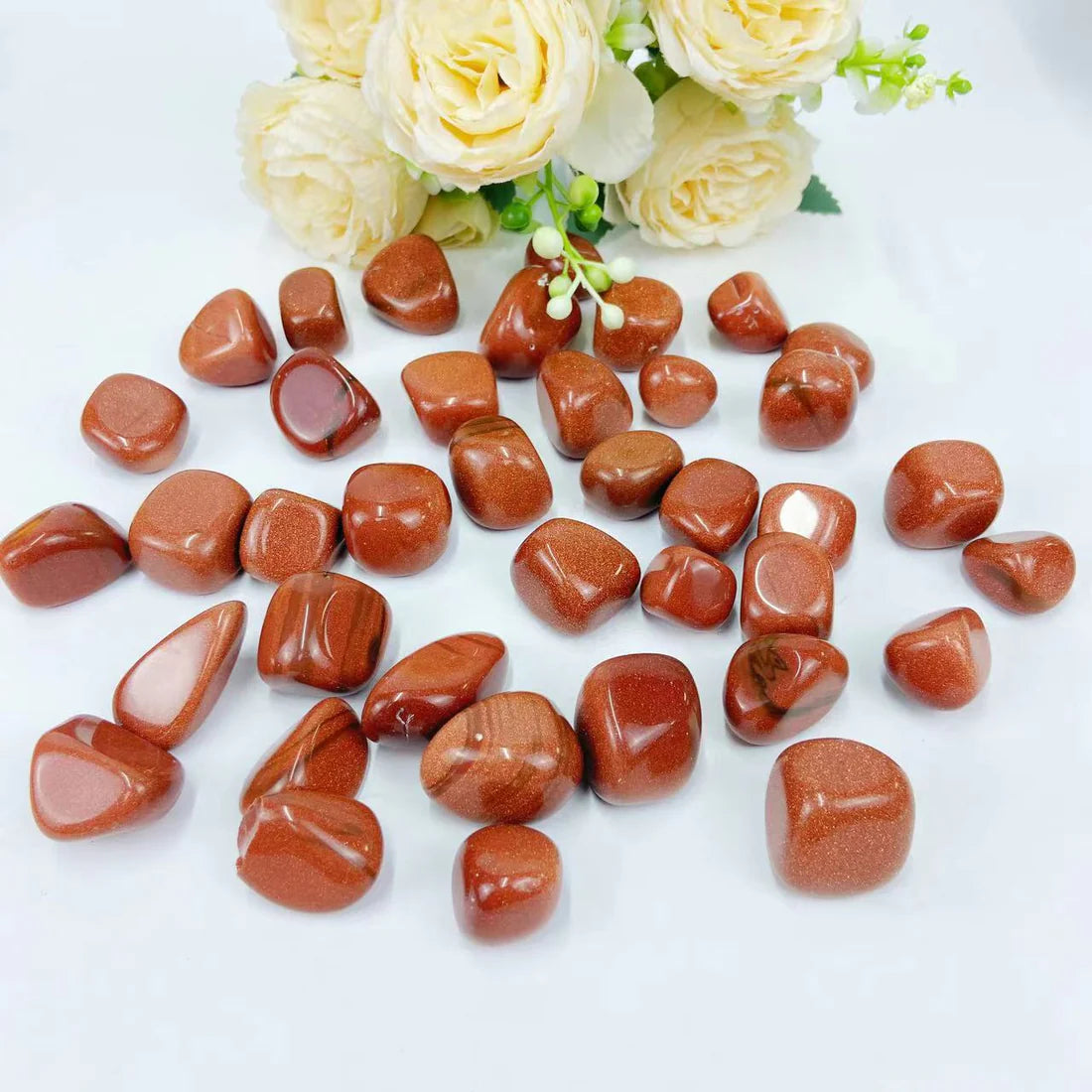 Gold Sandstone Crystal Tumbled Stones next to a bunch of yellow flowers.
