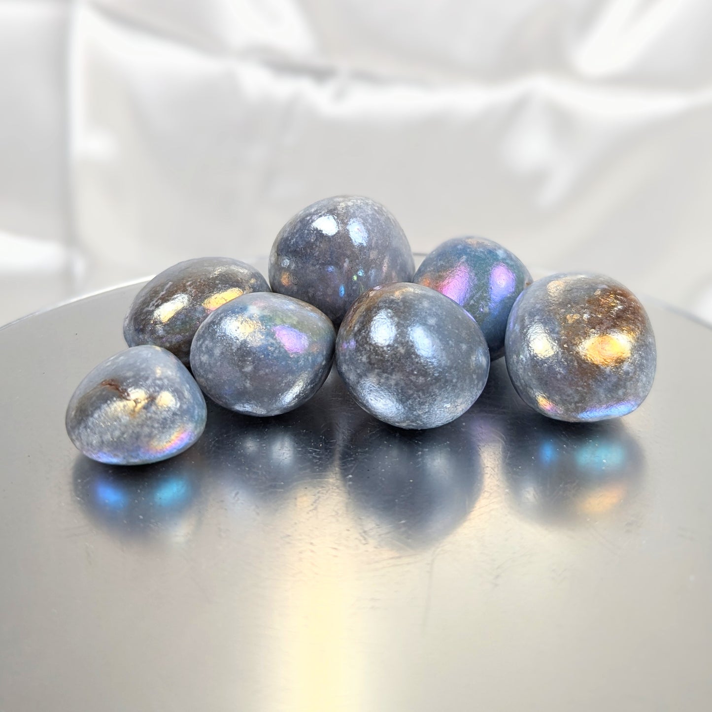 Angelite aura crystal tumblestones in a dappled grey with rainbow hues of pastel pink, blue and gold reflecting the light.