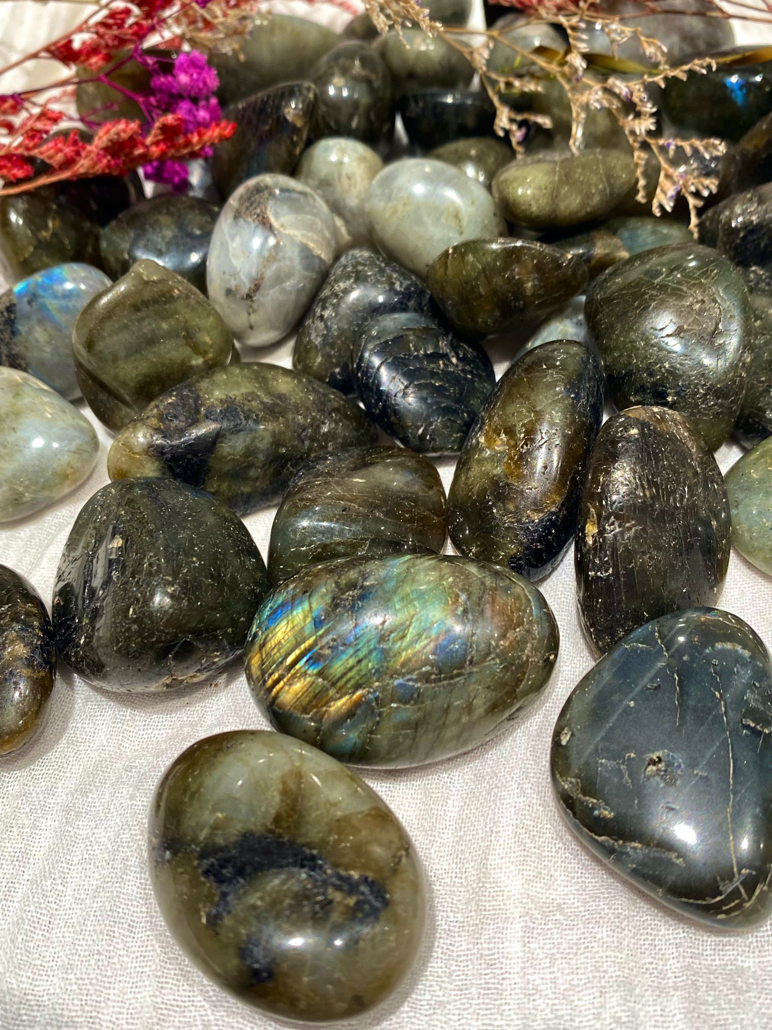 Medium labradorite tumblestones in dark green-browns, greys and pale beige, some with rainbow flecks in the light.