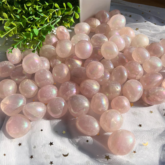 Rose quartz aura crystal tumblestones in pastel pink, glittering in rainbow colours where they catch the light.