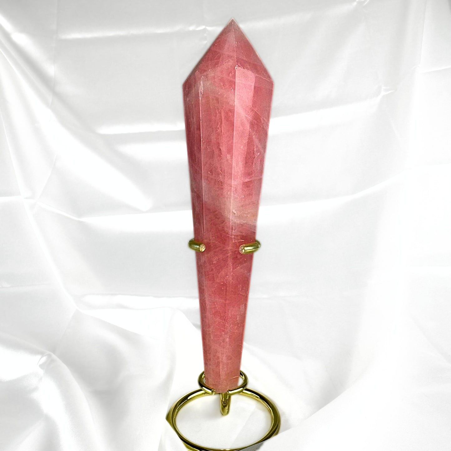The Rose Quartz Crystal healing wand, in vibrant pink tones with subtle white inclusions. The Rose Quartz wand is held in a golden wand display stand. 