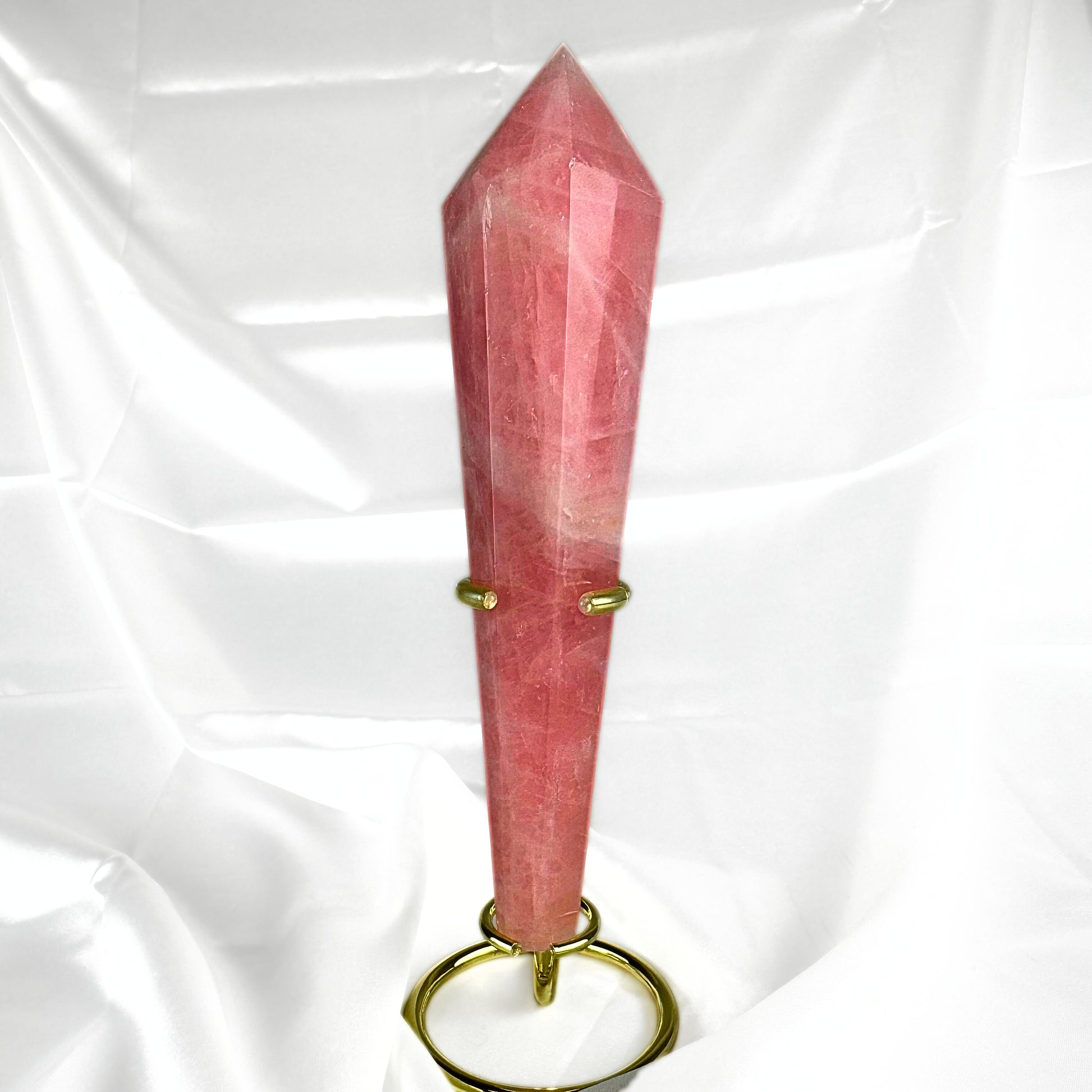 The Rose Quartz Crystal healing wand, in vibrant pink tones with subtle white inclusions. The Rose Quartz wand is held in a golden wand display stand. 